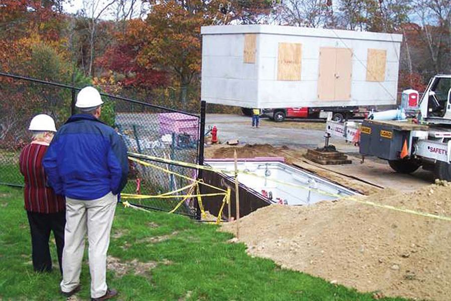 The self-contained pump station is lowered into position while Barnstable officials look on
